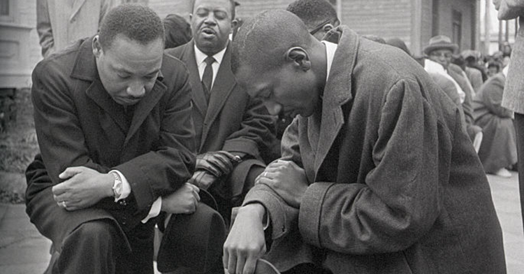 Civil rights leaders the Rev. Dr. Martin Luther King Jr. (left) and the Rev. Ralph Abernathy (center, rear) kneel with a group in prayer prior to going to jail in Selma, Alabama.