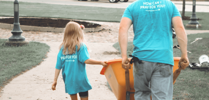 A man pushes a wheelbarrow while a young girl walks alongside