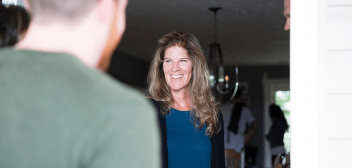 A smiling woman opens a door to let a person in