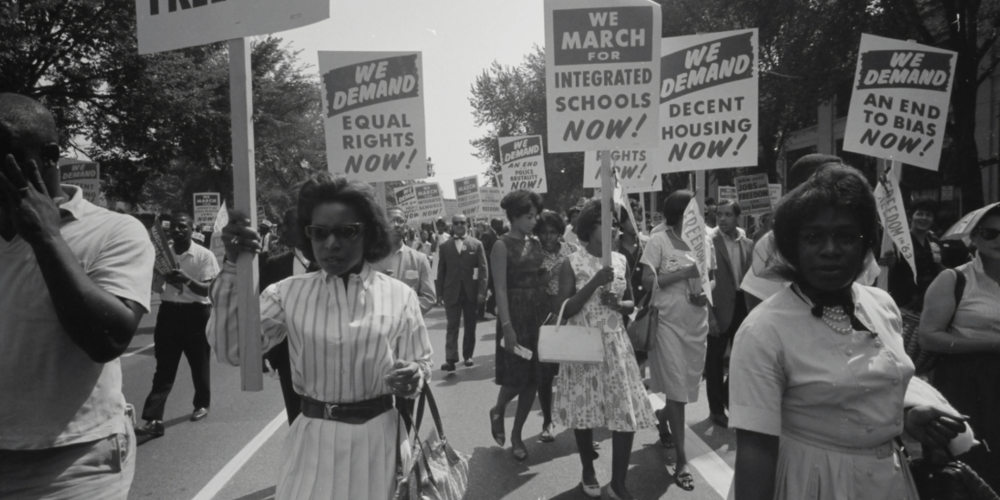 Image of protesters in a civil rights march holding signs with slogans like "We demand equal rights now!"