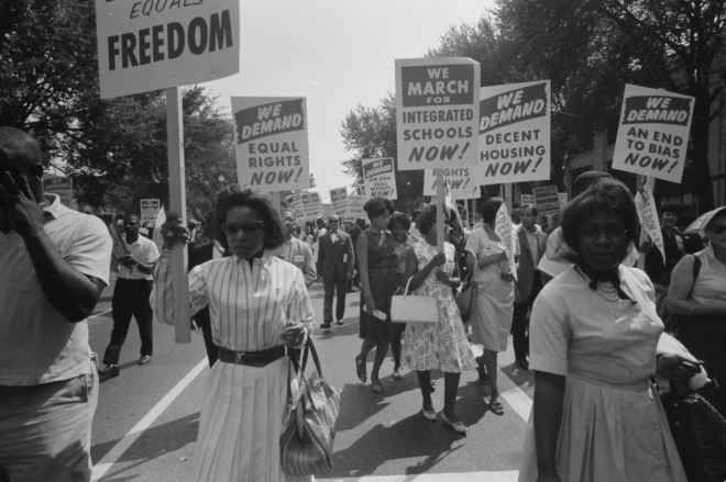 Image of protesters in a civil rights march holding signs with slogans like "We demand equal rights now!"