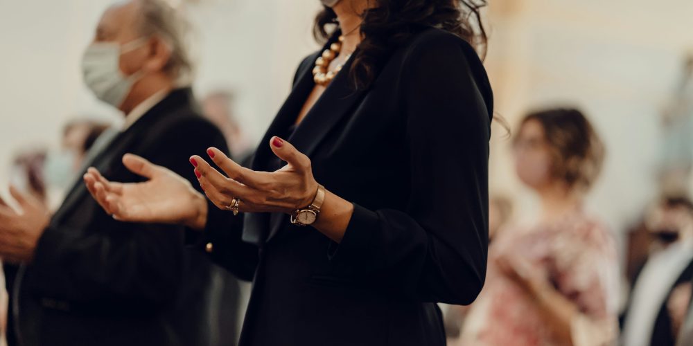 Woman wearing a mask in church prays with hands outstretched