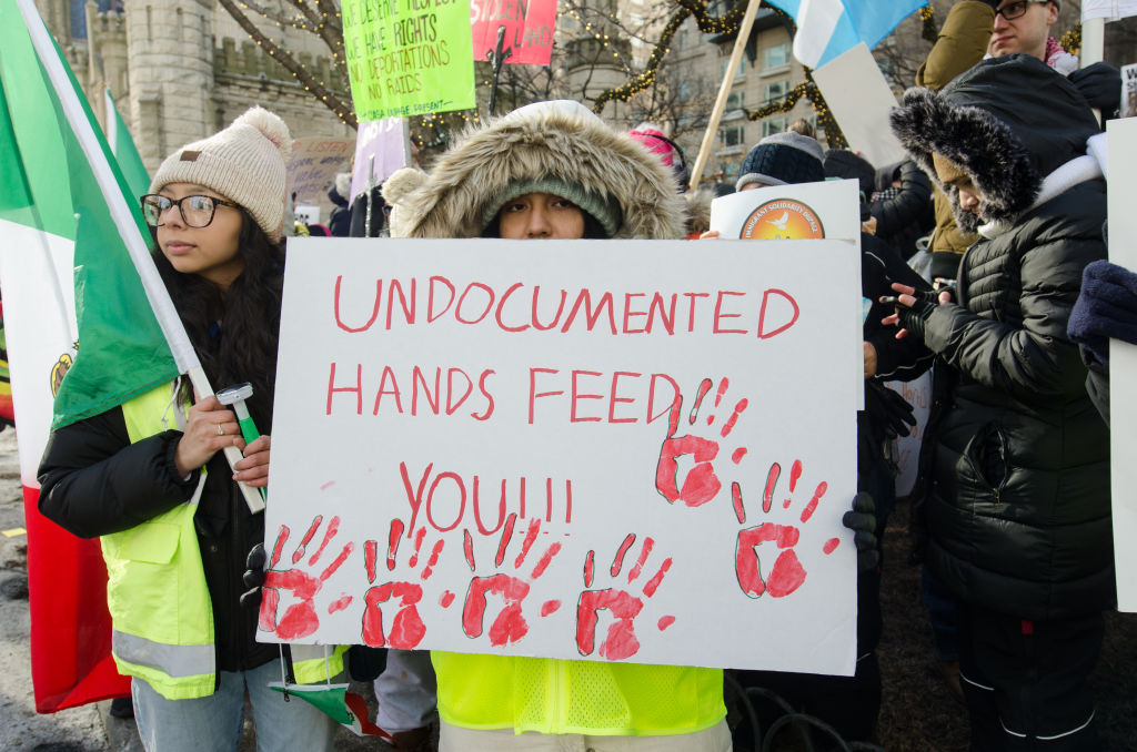 Protester holding a sign which reads "Undocumented hands feed you!!!"