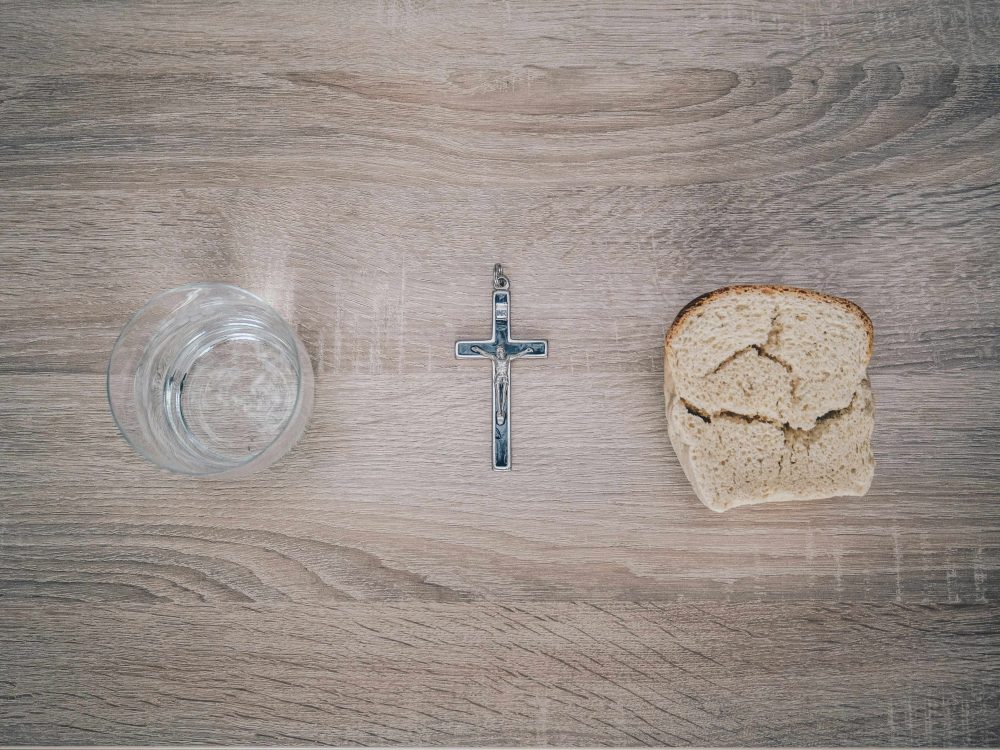 Two people climb up a snow-covered mountain A glass of water, a crucifix, and a piece of bread on a wood surface